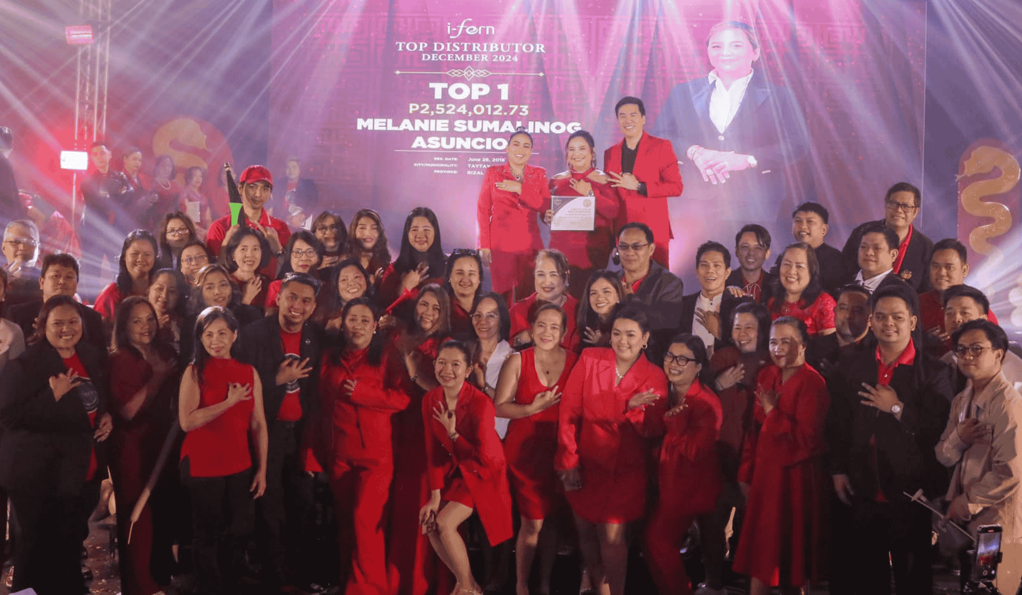 i-fern top distributor with i-fern Group of people in red and black outfits posing on a stage with bright lights and a large screen in the background contact i-ferndistributorusallc.com